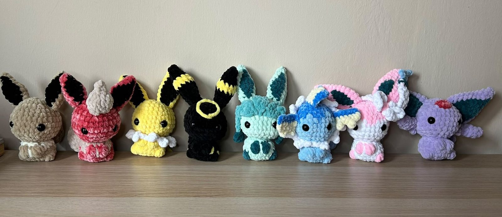 Otto peluche in ciniglia in fila su una mensola: Eevee e le sue evoluzioni in colori diversi