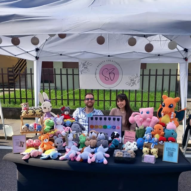 Il banchetto di SimpleBeauty Creations: un tavolo pieno di peluche all'uncinetto sotto un gazebo bianco con lo striscione del logo SB